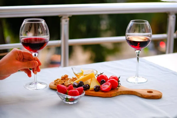 Balkondaki masada iki bardak kırmızı şarap ve peynir tabağı. Evde güzel yemekler..