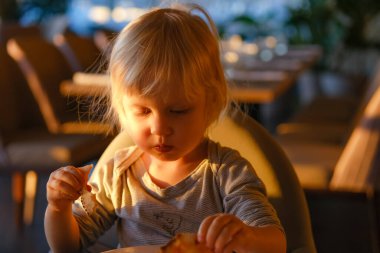 Küçük sarışın çocuk gün batımında restoranda pizza yiyor..