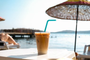 Ice latte coffee with a straw on the table. Man drinking coffee. Plastic cup of coffee on the beach.