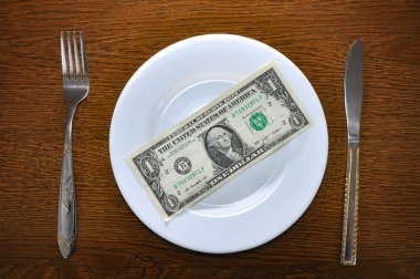 Beyaz bir tabağın üzerinde 1 Amerikan doları yatıyor. Fotoğraf, küresel ekonomide artan fiyatlar sorununu açıklıyor