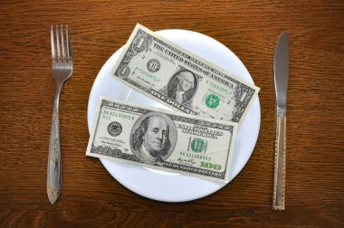 Beyaz bir tabakta 1 dolar ve 100 Amerikan doları var. Fotoğraf, küresel ekonomide artan fiyatlar sorununu açıklıyor