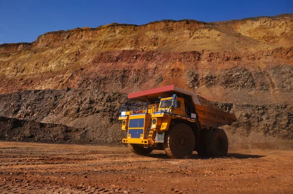 Mining dump truck transports rock, iron ore along the side of the quarry.