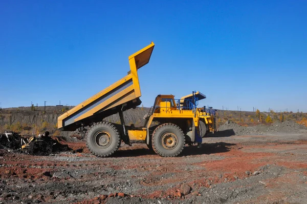 Mining dump truck transports rock, iron ore along the side of the quarry.