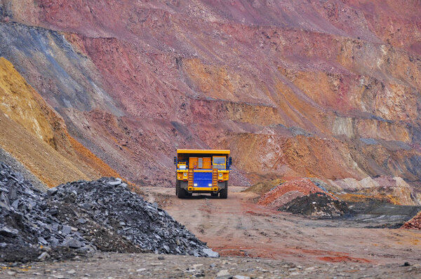 Extraction of iron ore. A mining dump truck transports iron ore along a side carrea. Special equipment works in a quarry. 