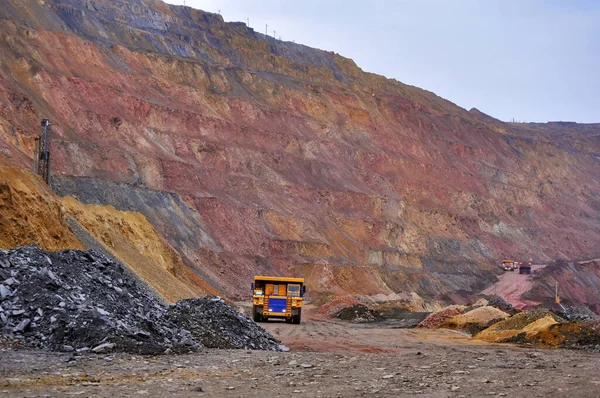 Extraction of iron ore. A mining dump truck transports iron ore along a side carrea. Special equipment works in a quarry.