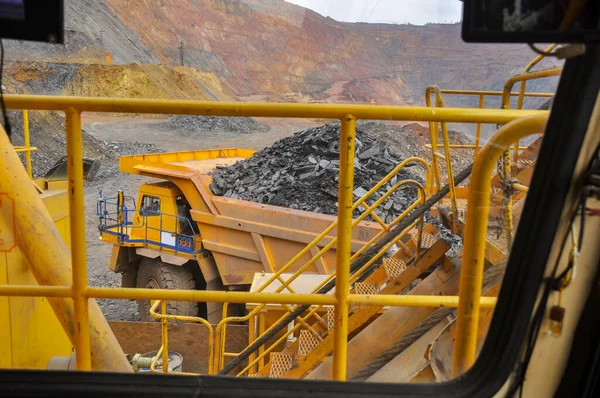 掘削機は鉄鉱石採石場のダンプトラックに鉄鉱石をロードします 掘削機の運転手のタクシーからの眺め — ストック写真