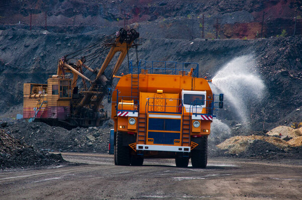 Тяжелый грузовик заливает дорогу водой в карьер железной руды. Удаление пыли, защита окружающей среды. Орошение дороги из пыли