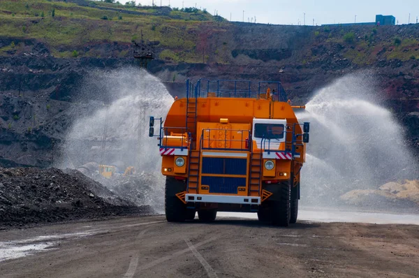 Heavy truck pours the road with water in the iron ore quarry. Dust removal, protection of the environment. Irrigation of the road from dust