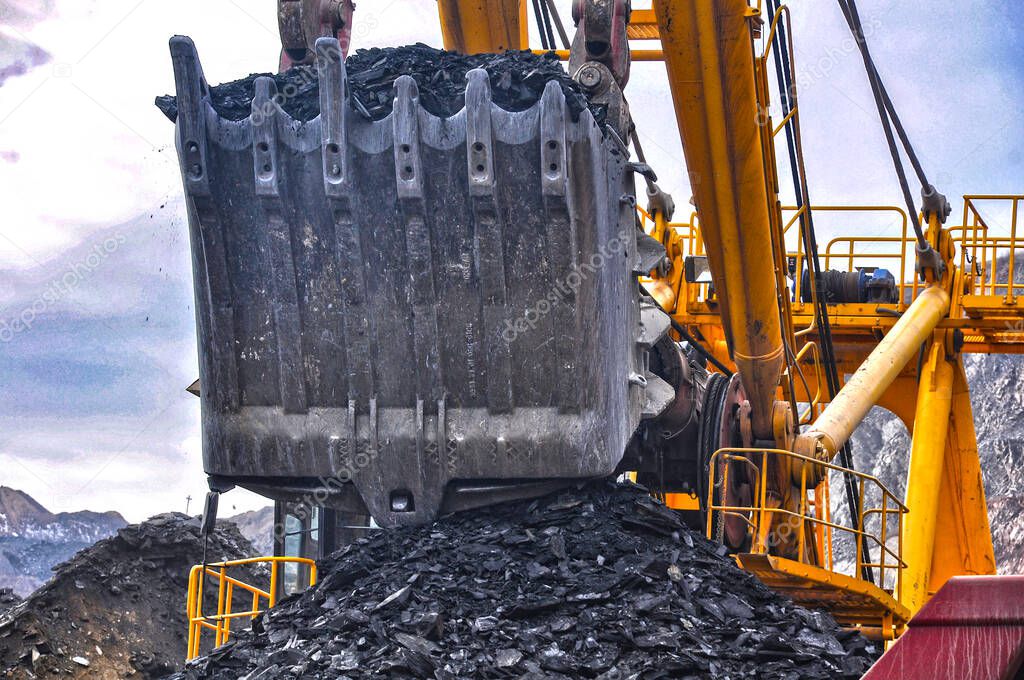 An excavator bucket loads iron ore into a dump truck. Close-up