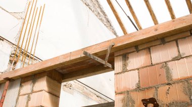 Arkasında ahşap çatı kirişleri olan bir inşaat alanının tuğla duvarı.