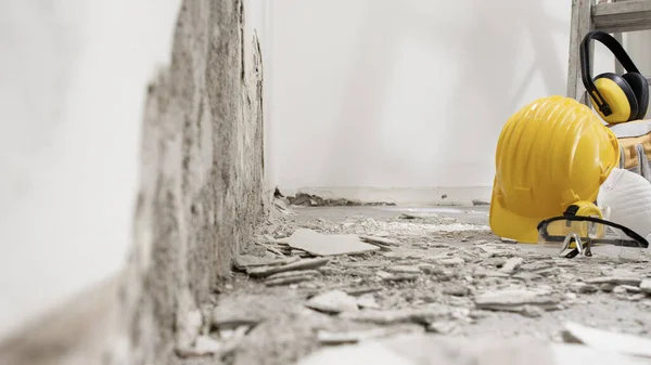 房屋翻新概念 带有灰泥瓦砾的拆墙和梯子上的防护施工工具 黄色头盔 白色背景的眼镜和耳机及复制空间 — 图库照片