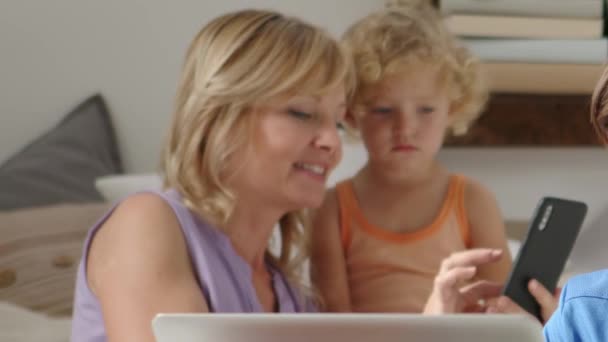 家里快乐的家庭 带着女儿和儿子的母亲在电脑和手机上玩得开心 在网上冲浪 在客厅里舒适地使用技术设备 社交媒体和现代生活方式 — 图库视频影像