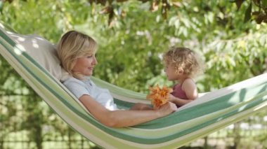 Mutlu anneler günü, gülümseyen anneler mavi gözlü küçük kızıyla oynuyorlar, kızı annesine bir nilüfer çiçeği veriyor, hamakta güneşli yeşil bahçede yatıyor, bahar ve yaz mevsimi konseptinde.