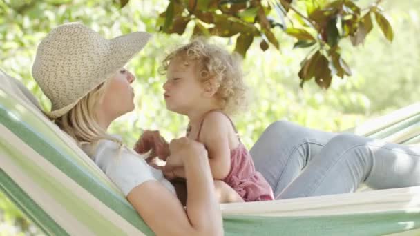 快乐的母亲节 笑着的妈妈和她的蓝眼睛小女孩玩着卷曲的金发 躺在吊床上 在阳光灿烂的花园里亲吻妈妈 春夏时节的概念 — 图库视频影像