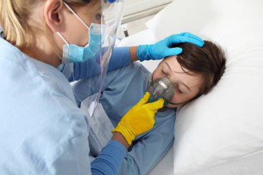 İnsani yardım, Ukrayna savaşı için tıbbi koruma, doktor hasta çocuğa hastane yatağında oksijen maskesi taktı, Ukrayna bayrağının sarı ve mavi eldiven renkleri. Yaralı Ukraynalı mülteciler