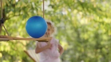 Happy family on sunny summer day. Little girl child daughter runs happy in the backyard lawn of house, playing with swing and balloon while her mother on the deck chair with laptop computer