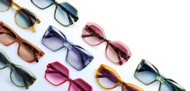 Sunglasses composition in many bright colors in transparent plastic. Top view with shadow. Trendy glasses isolated on white background. Glasses with polarized lenses. Fashionable eyewear for women.
