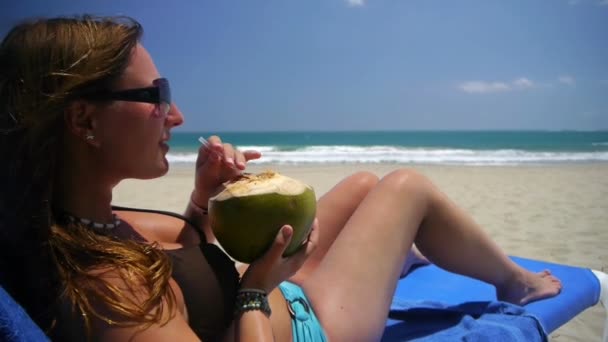 Дівчина п'є кокосове молоко на пляжі — стокове відео