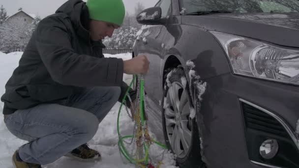 Homem tentando colocar correntes de neve em um carro — Vídeo de Stock