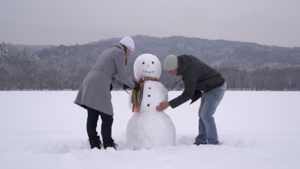 Casal jovem construindo um boneco de neve — Vídeo de Stock