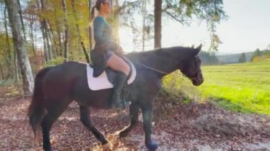 Genç kadın güzel atına binerek güneşli bir sonbahar gününün tadını çıkarıyor..