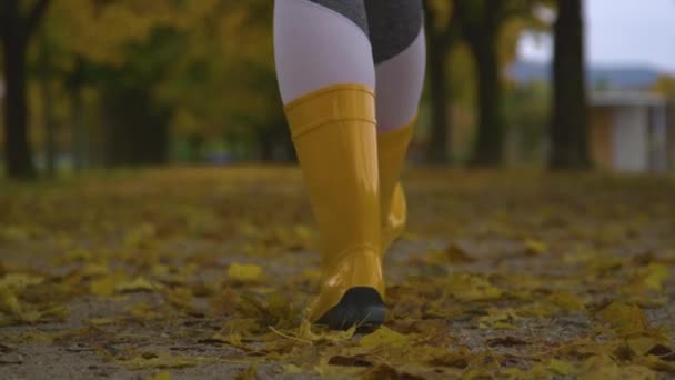 特写，道夫：穿着橡胶靴的女人走在长满树叶的大街上. — 图库视频影像