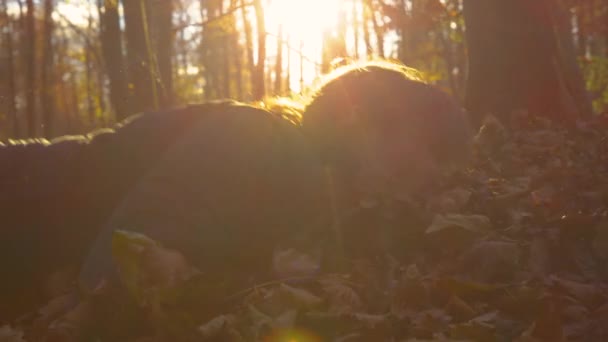 CLOSE UP: Young woman falls into pile of leaves while jogging in autumn forest. — Stock Video