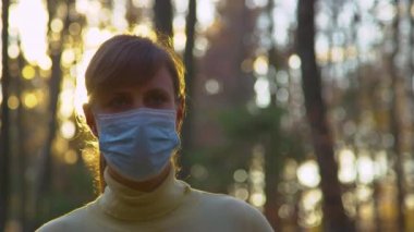 LENS FLARE Altın güneş ışıkları ormanda yürürken maske takan bir kadın üzerinde parlıyor.