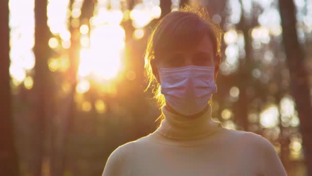 PORTRAIT: Female wearing a mask looks into camera during evening walk in woods. — Stock Video