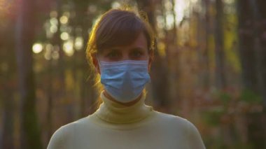 Altın gün batımı, yüzü maskeli bir kadın ormanı gezerken parlıyor..