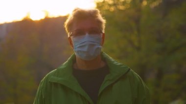 Gün batımı, yaşlı bir kadının yüz maskesi ile ormanı keşfetmesi üzerine parlıyor..