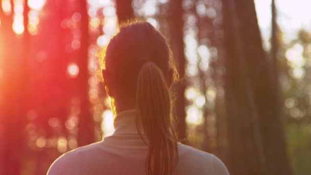 CLOSE UP: Gyllene solstrålar lyser på brunett kvinna som går på en promenad i skogen. — Stockvideo