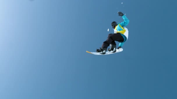 SLOW MOTION: Mannelijke toerist vliegt door de lucht en doet een snowboardtruc. — Stockvideo