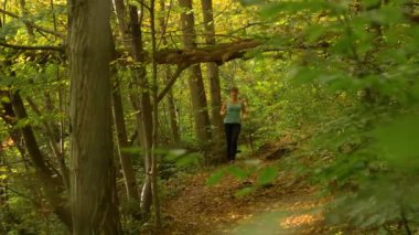 Formda bir kadın ormanda yürüyüş yaparken boş bir patika boyunca koşar..