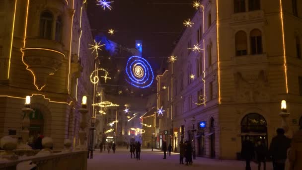 Tourists walk across the Ljubljana bridge ornated with bright Christmas lights. — Stockvideo