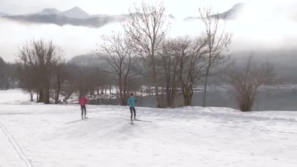 AERIAL: Twee jonge vrouwen trainen nordic skiën rond het spectaculaire meer Bohinj. — Stockvideo