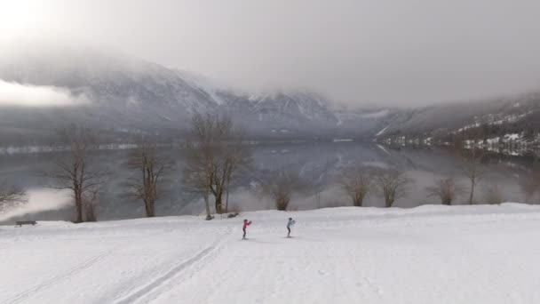 AERIAL: Twee vrouwelijke atleten Nordic skiën rond het adembenemende Bohinj meer. — Stockvideo