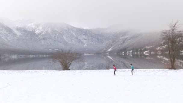 AERIAL: Volando a lo largo de atletas femeninas practicando esquí cerca del lago Bohinj. — Vídeo de stock