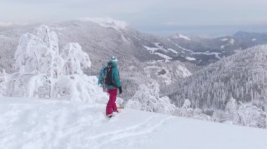 Genç bayan snowboardcu pistten ayrılmadan önce kışı seyrediyor..