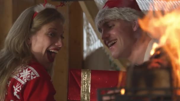 閉じる:クリスマスの日に暖炉でギフトを交換する幸せな若いカップル — ストック動画
