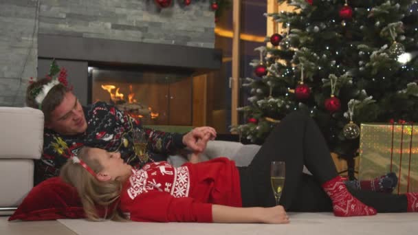 Affectionate young couple lying by the fireplace drinking wine on Christmas Eve — Stockvideo