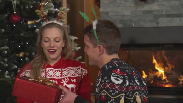 閉じる:クリスマスの夜に暖炉でギフトを交換する幸せな若いカップル — ストック動画