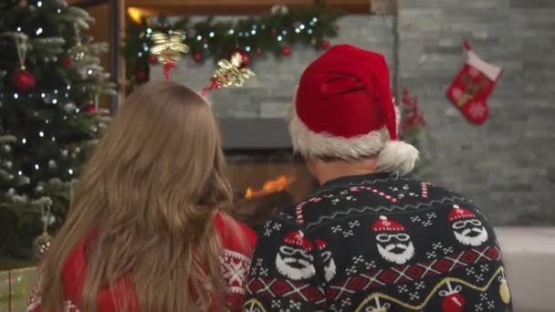 Pareja joven irreconocible cantando canciones de Navidad junto al fuego en casa — Vídeos de Stock