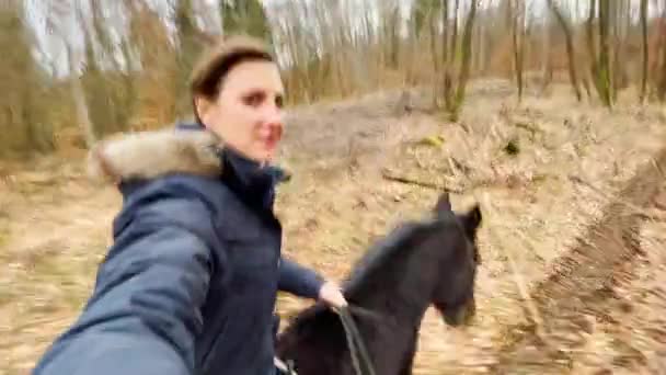 Μια νεαρή γυναίκα οδηγεί το άλογό της σε ένα μονοπάτι του δάσους μια κρύα φθινοπωρινή μέρα.. — Αρχείο Βίντεο