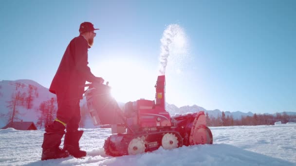 FLARE DE LA LENTE: Los rayos de sol brillantes brillan en un modelador masculino barbudo usando un soplador de nieve. — Vídeos de Stock