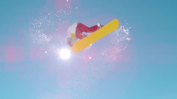 BOTTOM UP: Golden sunbeams shine on an extreme snowboarder doing a spinning grab — Stock videók