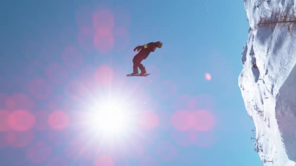 Parlak kış güneşleri, ters takla atan erkek bir snowboardcunun üzerinde parlıyor.. — Stok video
