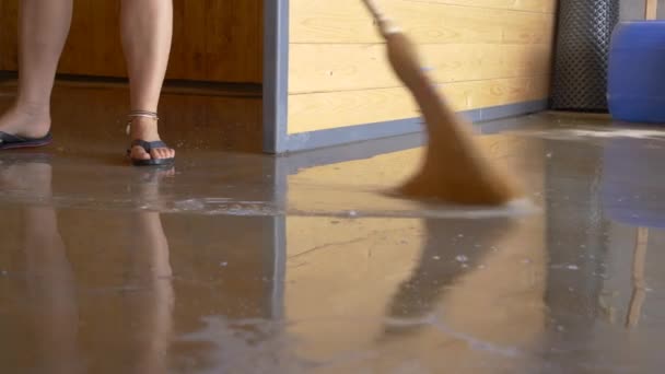 LOW ANGLE: Unrecognizable woman uses a straw broom to sweep the flooded floor. — Stockvideo