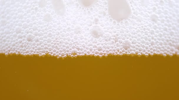 MACRO: Pequeñas burbujas forman la espuma encima de un vaso lleno de cerveza pálida. — Vídeos de Stock