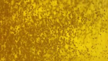 Minik karbondioksit kabarcıkları altın biranın etrafında yüzüyor ve bardağa dökülüyor..